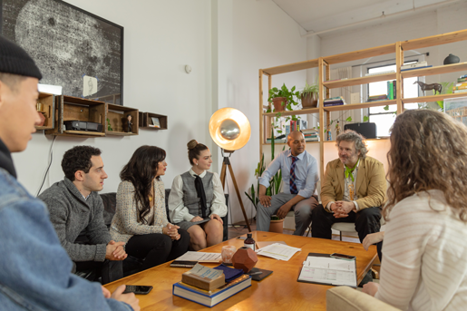 Photograph of a group of people meeting around a table with books and notepads.