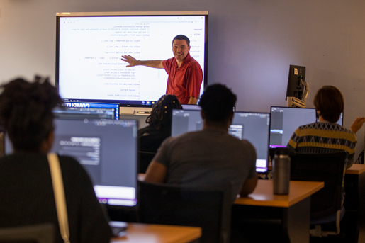 Photograph of an instructor gesturing towards a project in front of a class of students.